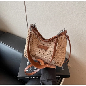 Detail of hand-held straw tote bag with brown leather trim and metal buckle accents