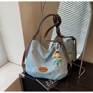 Détail du sac cabas en toile bleu clair avec lanières en cuir marron et pendentif dessin animé