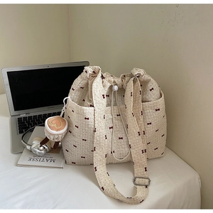 Detail of light beige floral tote with red bow pattern, drawstring and heart charm