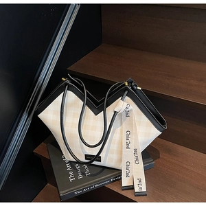 Close-up of a beige checkered tote bag with V-shaped opening on a wooden staircase