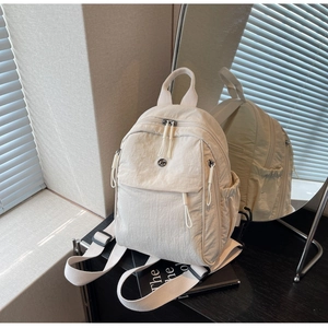 Detail of a lightweight cream nylon backpack with multiple pockets and zipper pulls