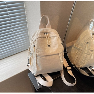 Detail of beige wrinkled nylon backpack showing multi-zipper pockets and metal logo