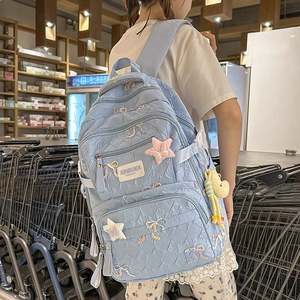 Detail of light blue quilted backpack with embroidered bows and plush bear charm