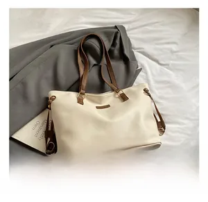 Detail of off-white tote bag with brown straps and metallic brand plate on bed