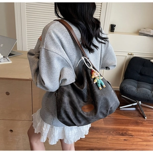 Détail du sac cabas en toile grise avec anses en cuir marron et pendentif poupée coloré