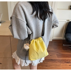 Détail d'un sac seau jaune vif à cordon avec un pompon en peluche et une bandoulière noire