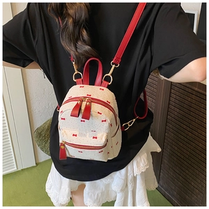 Detail of a sweet cream woven backpack with red bow prints and leather shoulder straps