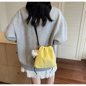 Sac seau jaune vif à cordon porté par un mannequin avec un charm de monstre en peluche