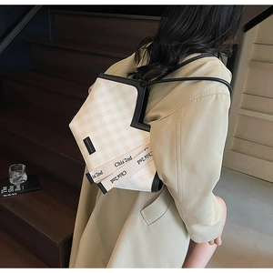 Detail view of checkered tote bag with branded wide strap on a wooden staircase