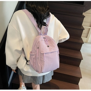 Rear view of a lavender nylon backpack being worn by a person on indoor stairs