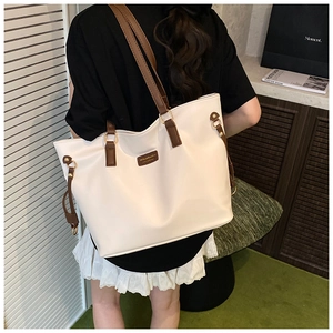 Detail of a large cream tote bag featuring brown leather straps and branded patch logo