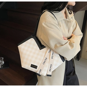 Detail of beige checkered canvas tote bag with black handles and woven logo strap