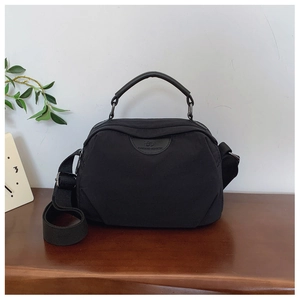 Dettaglio borsa a tracolla in nylon nero con manici in pelle e patch logo del marchio