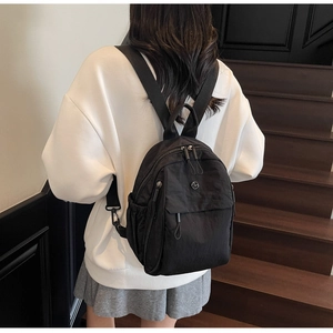 Close-up of a black nylon backpack on a model featuring multiple zipper pockets