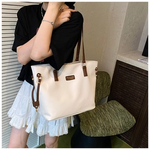 Detail of a large cream tote bag featuring brown contrast straps and fine leather texture