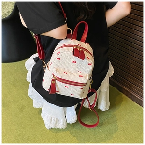 Mini white backpack with red bow patterns shown on model against a green background