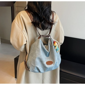 Détail d'un sac fourre-tout en toile bleu clair avec logo en cuir et pendentif poupée