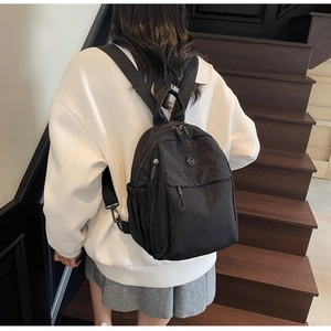 Detail of a lightweight black nylon backpack worn by a model on a wooden staircase