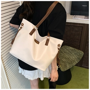 Detail of cream tote bag featuring brown shoulder straps and reinforced stitching