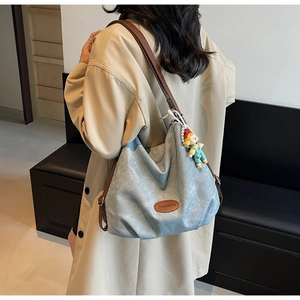 Détail du sac fourre-tout bleu clair avec anses en cuir marron et accessoire poupée mignonne