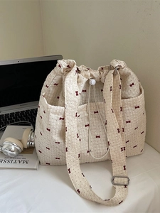 Cream canvas tote bag with red bow print and drawstring closure on a desk with laptop