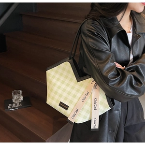 Detail of green gingham tote bag featuring a branded strap and a black faux leather trim