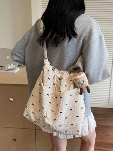 Off-white canvas tote bag with red bow print, drawstring closure, and smiley plush charm