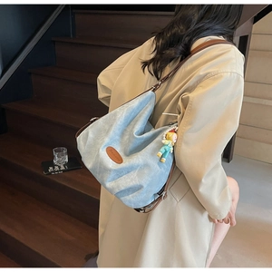 Détail d'un sac fourre-tout en jean bleu clair avec bandoulière en cuir et charm poupée