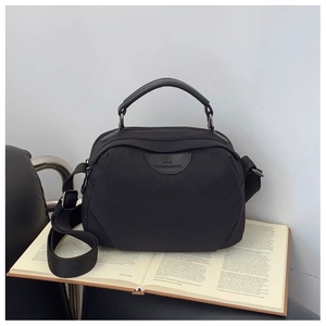 Dettaglio della borsa a tracolla in nylon nero su un libro con manico in pelle e logo