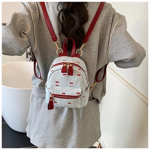 Detailed view of mini woven backpack featuring red bow embroidery and red straps