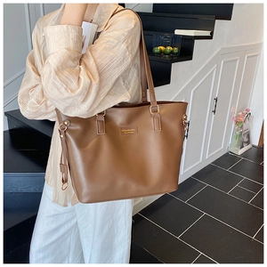 Deep brown tote bag with gold charm worn by model in a minimalist indoor setting