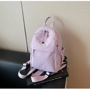 Detailed view of lavender nylon mini backpack on art books showing front flap pocket and logo