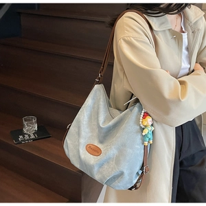 Détail du cabas bleu-gris avec logo en cuir et chaîne décorative en perles sur la sangle
