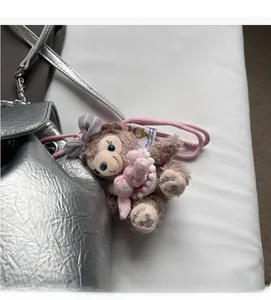 Detail eines Plüschbären mit rosa Schleife und Perlenkette an einem Metallic-Rucksack