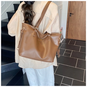 Close-up of large brown tote bag with leather texture and metal buckle detail on the side