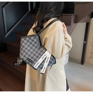 Detail of checkered tote bag with branded strap worn with a beige trench coat