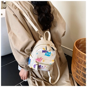 Close-up of a white mini backpack with cute cat graffiti worn with a beige trench coat