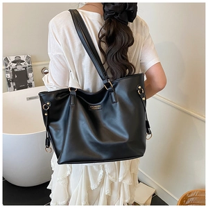 Detailed back view of a large black faux leather tote bag with gold metal logo on a model