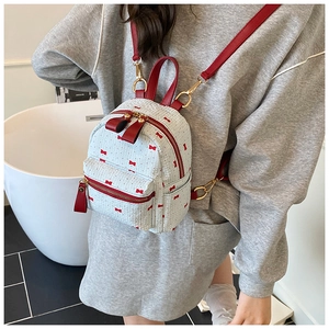 Detail of mini backpack showing red bow print on white plaid fabric with metal hardware