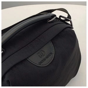 Dettaglio della borsa in nylon nero con tracolla, clip metalliche e patch logo tonda