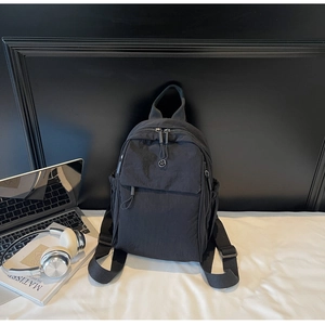 Minimalist black nylon backpack with a laptop and headphones in a lifestyle setting