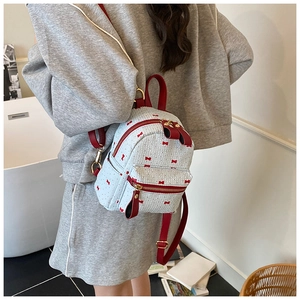 Close-up of light blue mini backpack with red bow print and leather straps detail