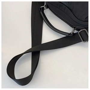 Dettaglio della borsa in nylon nero con manico in pelle e fibbia metallica sulla tracolla
