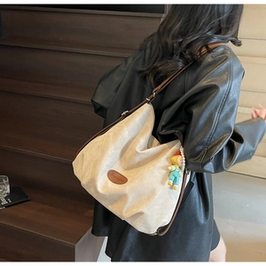 Détail d'un sac cabas blanc cassé avec bandoulière en cuir marron et logo sur un mannequin
