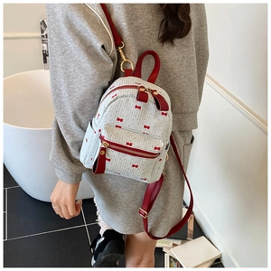 Close-up of white woven backpack featuring red bow patterns and golden zipper details