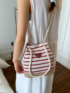 Borsa a secchiello in tela a righe con fondo in paglia indossata da una modella