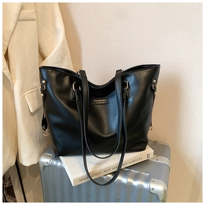 Detail of a large black PU leather tote bag with gold hardware on white books
