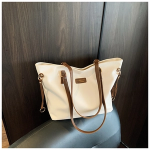 Detail of white tote bag with brown straps and side drawstring on dark leather seat