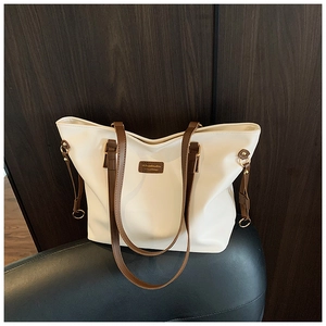 Detail of off-white tote bag with dark brown leather handles and brand logo patch