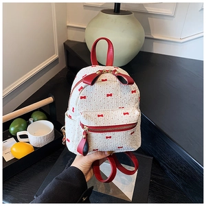 Detail of mini backpack with red bow print and leather handles held in hand